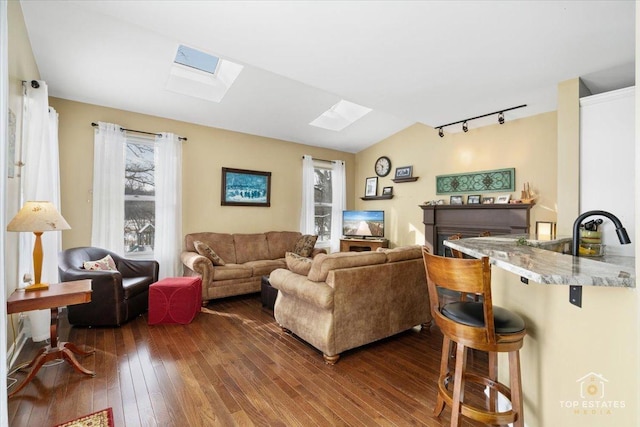 living room with vaulted ceiling with skylight, dark wood-style floors, and track lighting