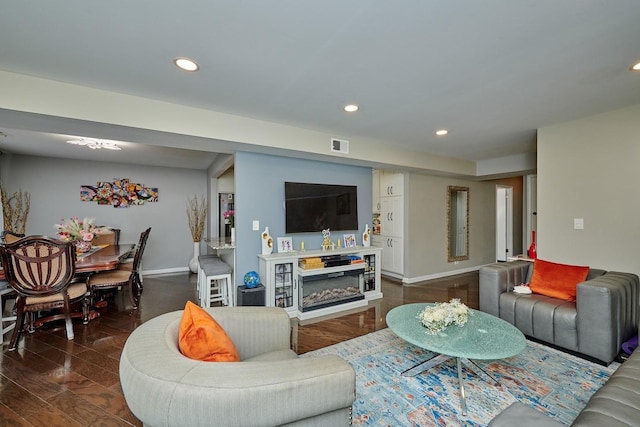 living area featuring a glass covered fireplace, visible vents, baseboards, and recessed lighting