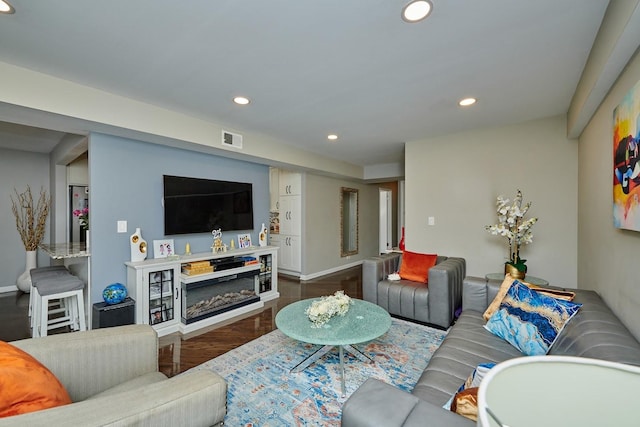 living area featuring baseboards, visible vents, a glass covered fireplace, wood finished floors, and recessed lighting