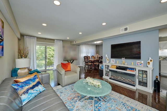 living area with a glass covered fireplace, wood finished floors, visible vents, and recessed lighting