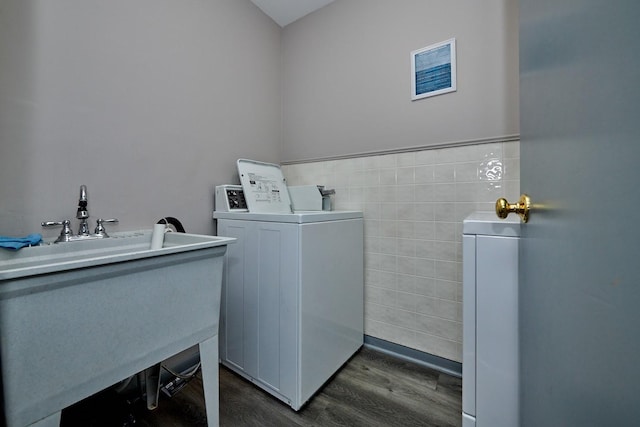 washroom featuring tile walls, dark wood-type flooring, washing machine and dryer, wainscoting, and a sink