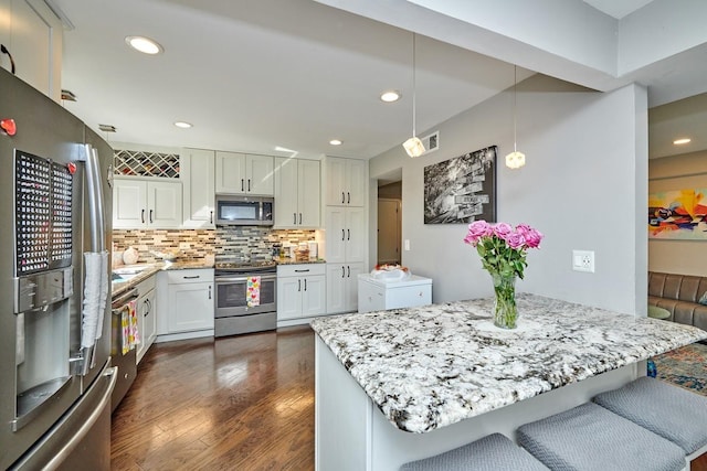 kitchen with stainless steel appliances, tasteful backsplash, dark wood-type flooring, white cabinetry, and light stone countertops