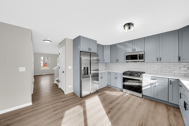 kitchen with tasteful backsplash, gray cabinetry, stainless steel appliances, and light countertops