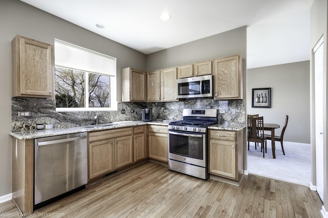 kitchen featuring light brown cabinets, a sink, stainless steel appliances, tasteful backsplash, and light wood-type flooring