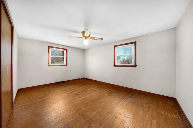 spare room featuring baseboards, wood-type flooring, visible vents, and a wealth of natural light