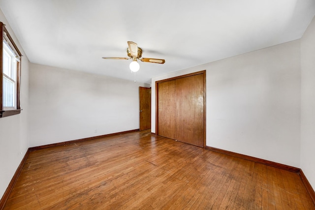 unfurnished bedroom featuring hardwood / wood-style floors, a closet, a ceiling fan, and baseboards