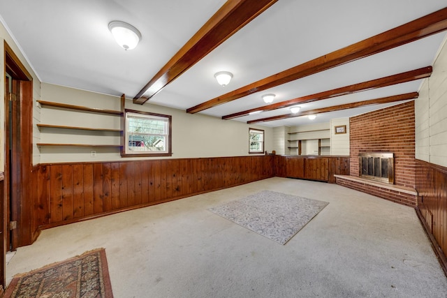 unfurnished living room featuring wood walls, wainscoting, a brick fireplace, beam ceiling, and carpet