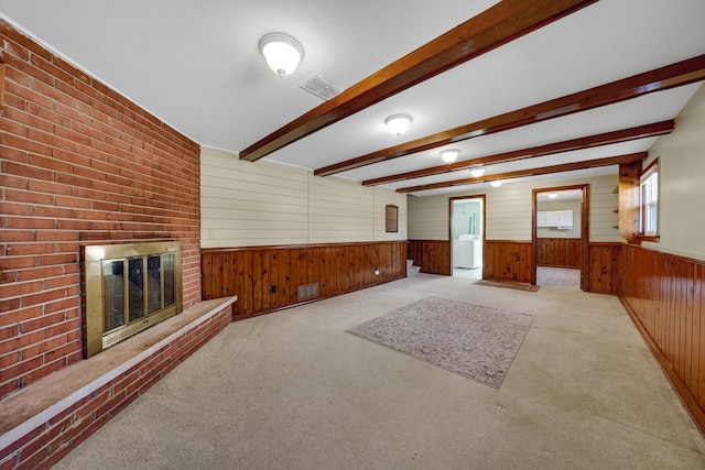 unfurnished living room with carpet floors, wood walls, a fireplace, visible vents, and beam ceiling