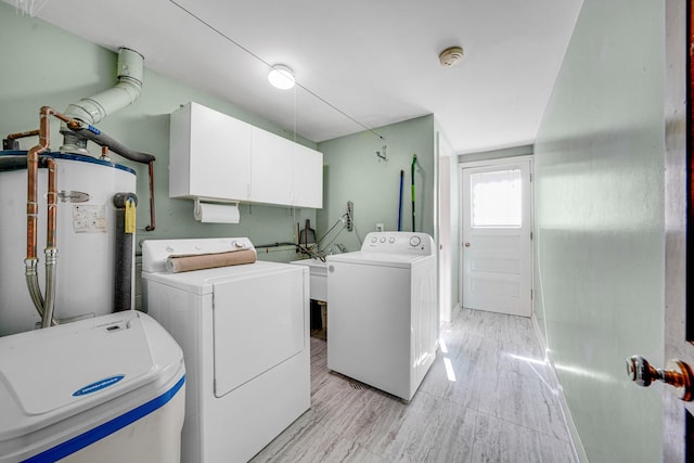 washroom featuring water heater, light wood-type flooring, washing machine and clothes dryer, and cabinet space