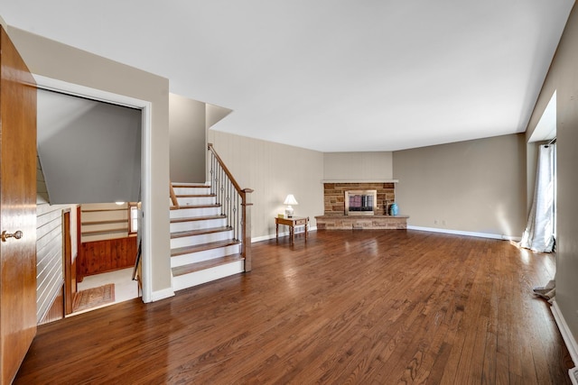 living room with a stone fireplace, stairway, wood-type flooring, and baseboards