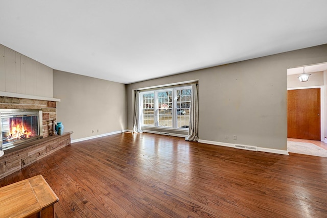 unfurnished living room featuring baseboards, visible vents, wood finished floors, and a stone fireplace