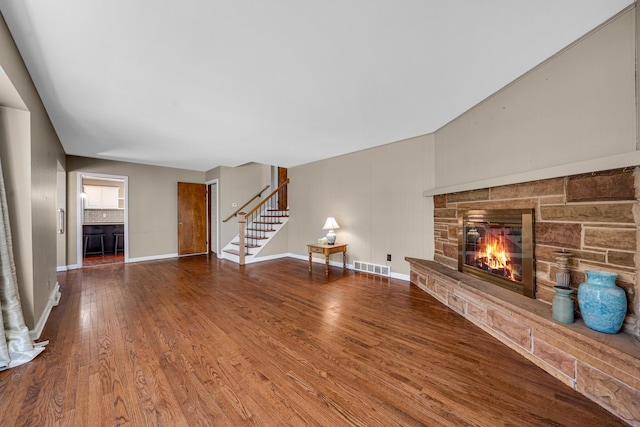 unfurnished living room featuring baseboards, visible vents, wood finished floors, stairs, and a fireplace