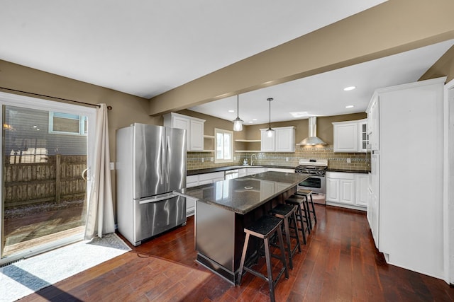 kitchen with dark wood-style floors, wall chimney exhaust hood, a kitchen island, stainless steel appliances, and open shelves