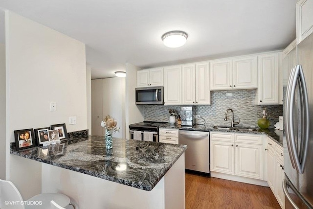 kitchen featuring dark stone countertops, appliances with stainless steel finishes, a peninsula, and a sink