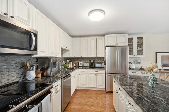 kitchen featuring a sink, decorative backsplash, glass insert cabinets, light wood-style floors, and appliances with stainless steel finishes