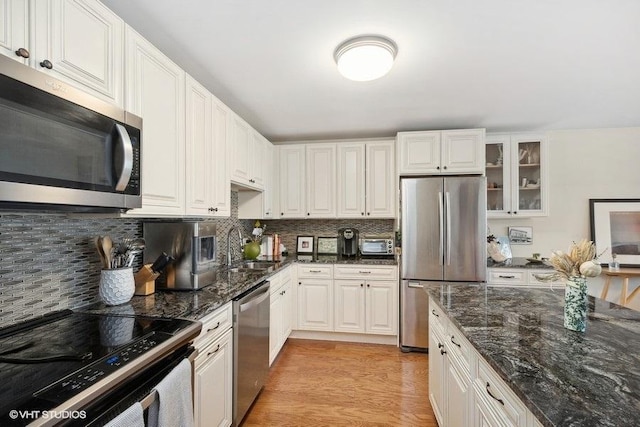 kitchen featuring light wood-style flooring, a sink, tasteful backsplash, appliances with stainless steel finishes, and glass insert cabinets