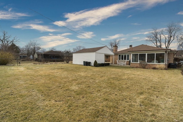 back of house featuring a sunroom, an outbuilding, fence, a yard, and brick siding