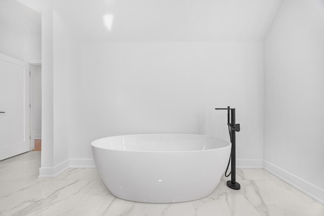 bathroom featuring marble finish floor, a freestanding bath, and baseboards