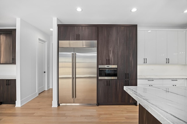 kitchen with light stone counters, dark brown cabinetry, stainless steel appliances, white cabinets, and light wood-type flooring