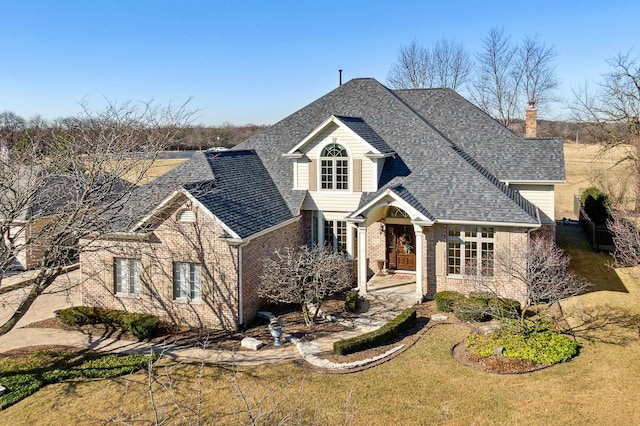 view of front of home featuring brick siding, roof with shingles, and a front yard