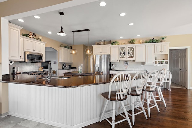 kitchen with dark countertops, a peninsula, arched walkways, stainless steel appliances, and a sink