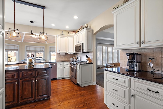 kitchen with dark wood-style floors, arched walkways, appliances with stainless steel finishes, white cabinetry, and backsplash