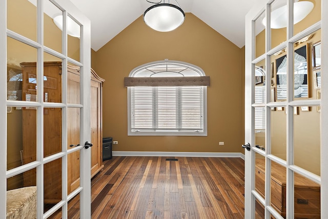 empty room featuring french doors, baseboards, lofted ceiling, and hardwood / wood-style floors