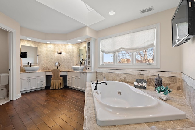 full bath featuring visible vents, a whirlpool tub, a skylight, wood finished floors, and vanity