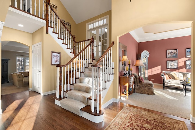 stairway featuring baseboards, arched walkways, high vaulted ceiling, and wood finished floors