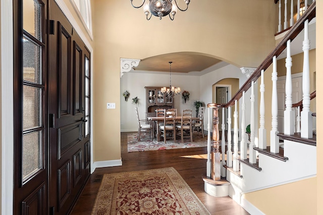 entryway with dark wood-type flooring, stairway, a high ceiling, arched walkways, and a notable chandelier