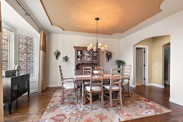 dining space with baseboards, an inviting chandelier, arched walkways, hardwood / wood-style flooring, and a raised ceiling