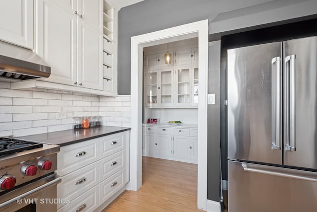 kitchen with under cabinet range hood, high quality appliances, decorative backsplash, light wood-style floors, and white cabinets