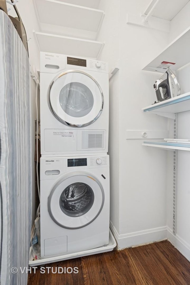 clothes washing area featuring laundry area, wood finished floors, baseboards, and stacked washing maching and dryer