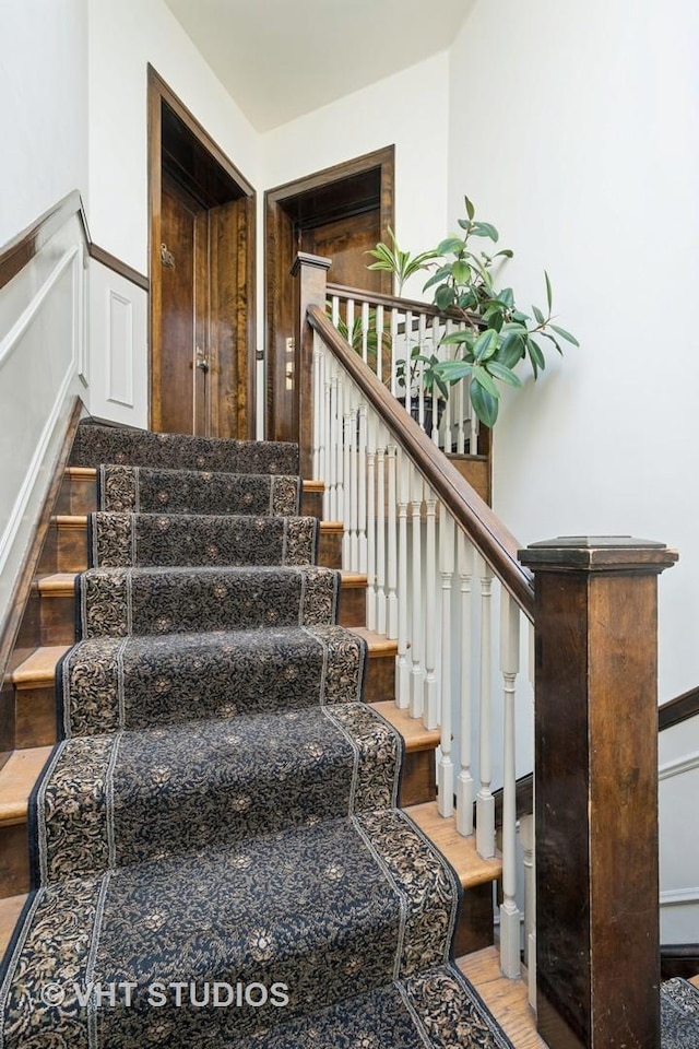 stairway featuring wood finished floors, wainscoting, and a decorative wall