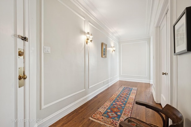 corridor with wood finished floors, ornamental molding, and a decorative wall