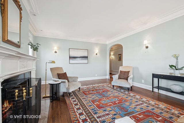 living area with ornamental molding, a warm lit fireplace, wood finished floors, arched walkways, and baseboards