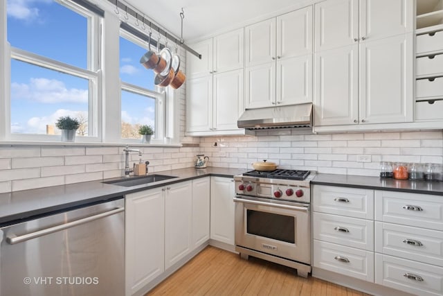 kitchen featuring a sink, under cabinet range hood, appliances with stainless steel finishes, white cabinetry, and dark countertops