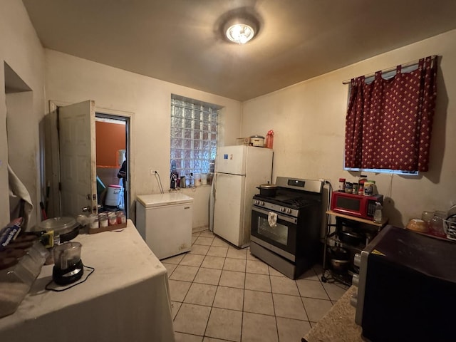 kitchen featuring freestanding refrigerator, fridge, stainless steel range with gas cooktop, light tile patterned flooring, and light countertops