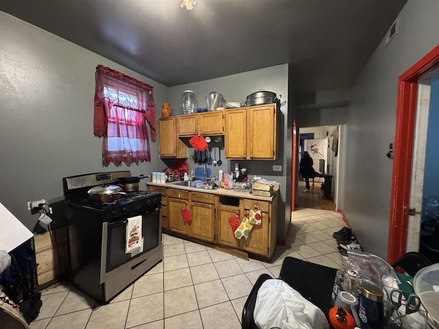 kitchen with stainless steel range with gas stovetop, light countertops, light tile patterned floors, brown cabinetry, and a sink