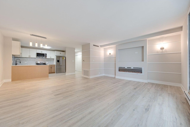 unfurnished living room featuring light wood-style floors, baseboards, a sink, and a glass covered fireplace