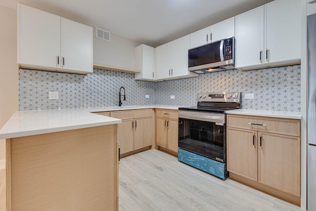 kitchen featuring light brown cabinets, stainless steel appliances, a sink, visible vents, and light wood-style floors