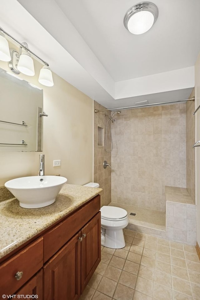 bathroom featuring toilet, vanity, a tile shower, and tile patterned floors