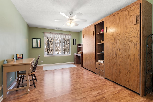 office with a textured ceiling, light wood finished floors, visible vents, and a ceiling fan