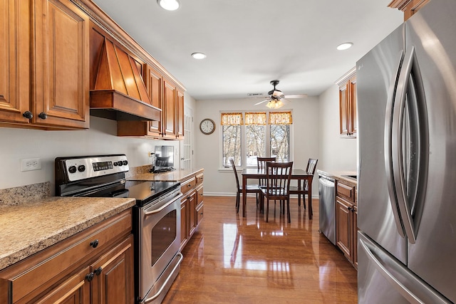 kitchen with stainless steel appliances, brown cabinetry, premium range hood, and baseboards