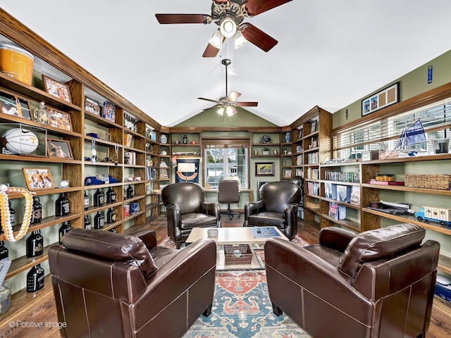 office area with ceiling fan, wood finished floors, wall of books, and vaulted ceiling