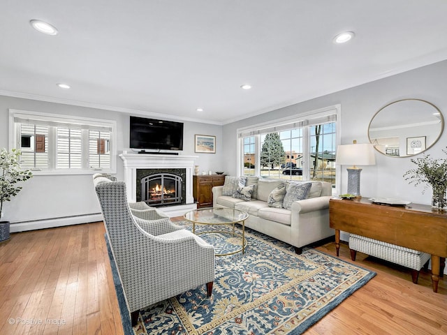 living area with crown molding, a baseboard heating unit, recessed lighting, a glass covered fireplace, and wood-type flooring