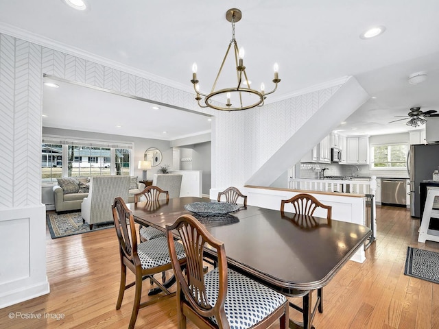 dining space with light wood-style flooring, ornamental molding, ceiling fan with notable chandelier, recessed lighting, and wallpapered walls