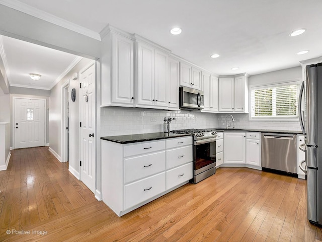 kitchen with ornamental molding, dark countertops, white cabinetry, light wood-style floors, and appliances with stainless steel finishes