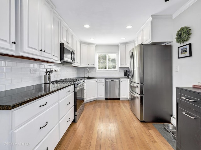 kitchen featuring light wood-style flooring, a sink, backsplash, white cabinetry, and appliances with stainless steel finishes