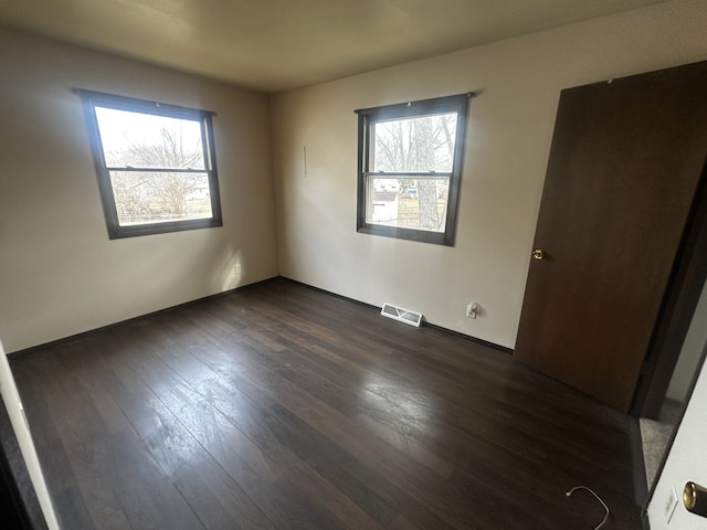 unfurnished bedroom with dark wood-style flooring, visible vents, and multiple windows